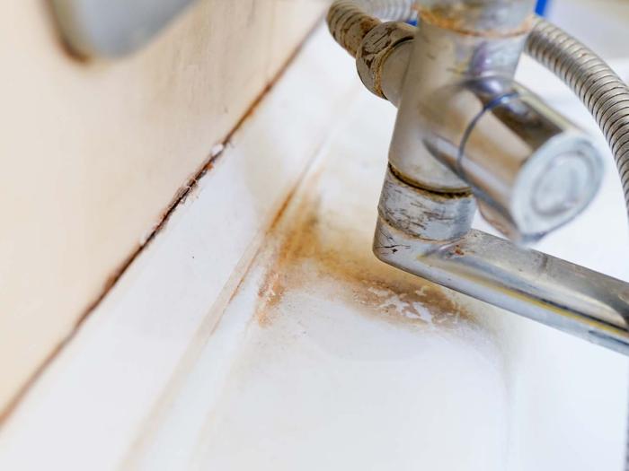 Zacieki z rdzy wokół baterii łazienkowej na umywalce ceramicznej